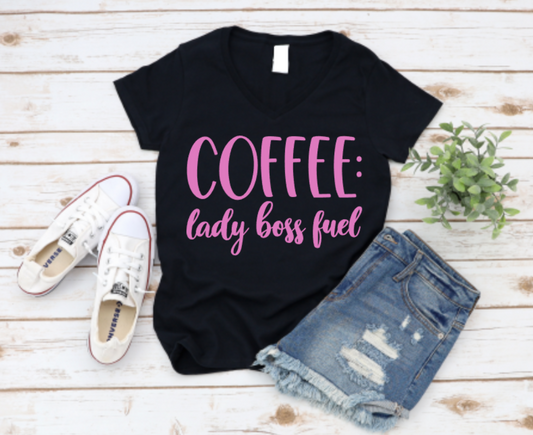 Black t-shirt with bold black “Coffee: lady boss fuel” text, styled with ripped denim shorts and white Converse sneakers on a white wooden background.