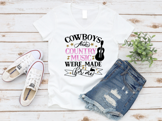 White t-shirt with "Cowboys and Country Music Were Made for Me" graphic, featuring stars, a guitar, and musical notes, styled with denim shorts and white Converse on a wooden background.