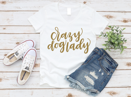 White t-shirt with “Crazy Dog Lady” text in gold, paired with white Converse sneakers and ripped denim shorts on a light wooden background.