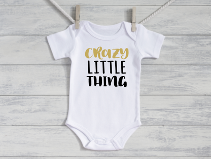 White baby onesie with 'Crazy Little Thing' text on a wooden surface