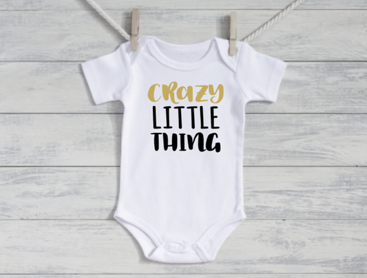 White baby onesie with 'Crazy Little Thing' text on a wooden surface