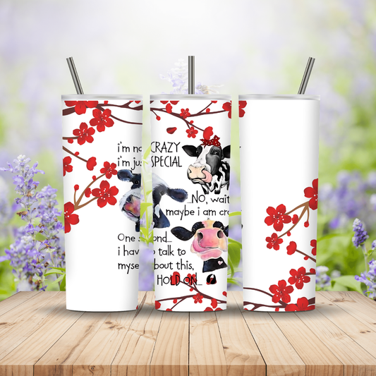 Three tumblers with cow designs and floral patterns on a wooden surface with a blurred natural background.