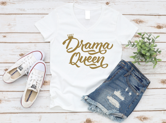 White t-shirt with “Drama Queen” in bold gold script, styled with ripped denim shorts and white Converse sneakers on a light wood background.