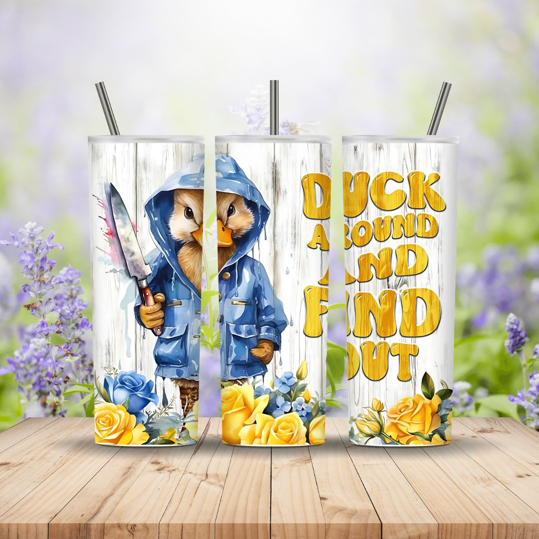 Two tumblers with a duck in a raincoat design and text on a wooden surface with flowers.