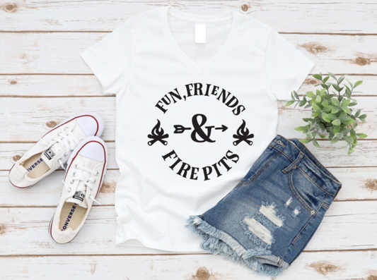 White v-neck t-shirt with “Fun, Friends & Fire Pits” graphic in white, styled flat lay with denim shorts, white Converse sneakers, and a plant on a wood background.
