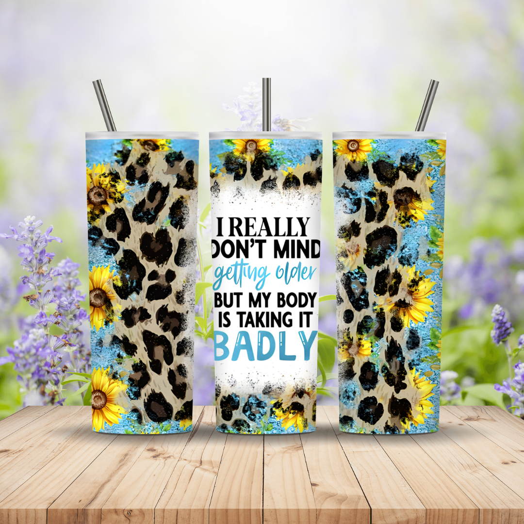Three tumblers with leopard print and sunflower design on a wooden surface with a blurred floral background.