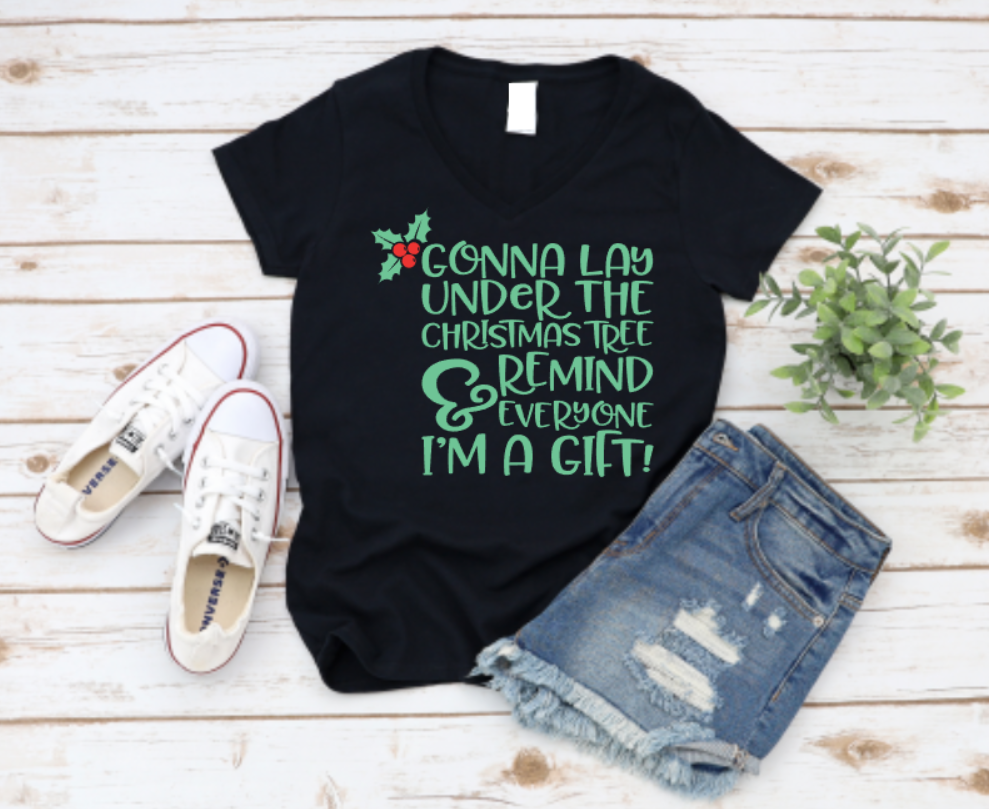 Black t-shirt with Christmas-themed text, paired with denim shorts and white sneakers on a wooden surface.