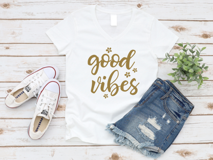 White t-shirt with 'good vibes' text, white sneakers, and denim shorts on a wooden surface.