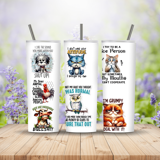 Three tumbler cups with animal-themed designs and humorous text on a wooden surface with a blurred floral background.
