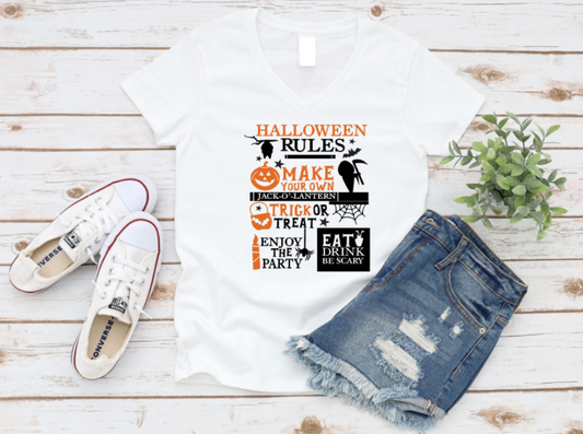 White t-shirt with Halloween-themed design, denim shorts, and white sneakers on a wooden surface.