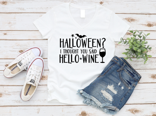 White t-shirt with 'Halloween? I thought you said hello wine' text, white sneakers, and denim shorts on a wooden surface.