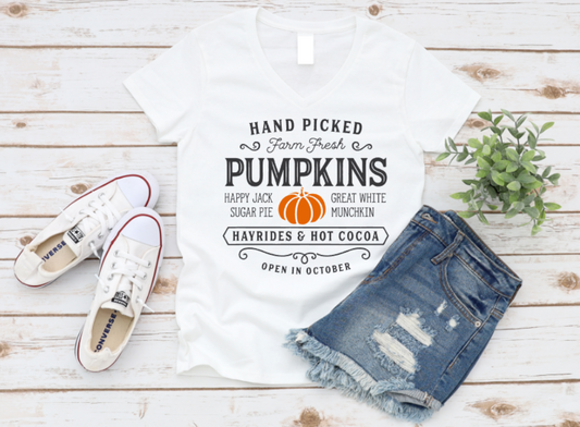 White pumpkin shirt with text, white sneakers, and denim shorts on a wooden surface.