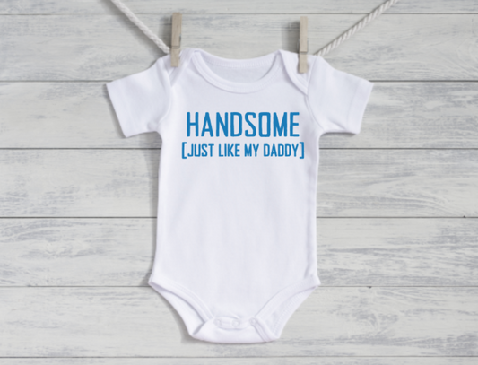 White baby onesie with blue text on a wooden surface
