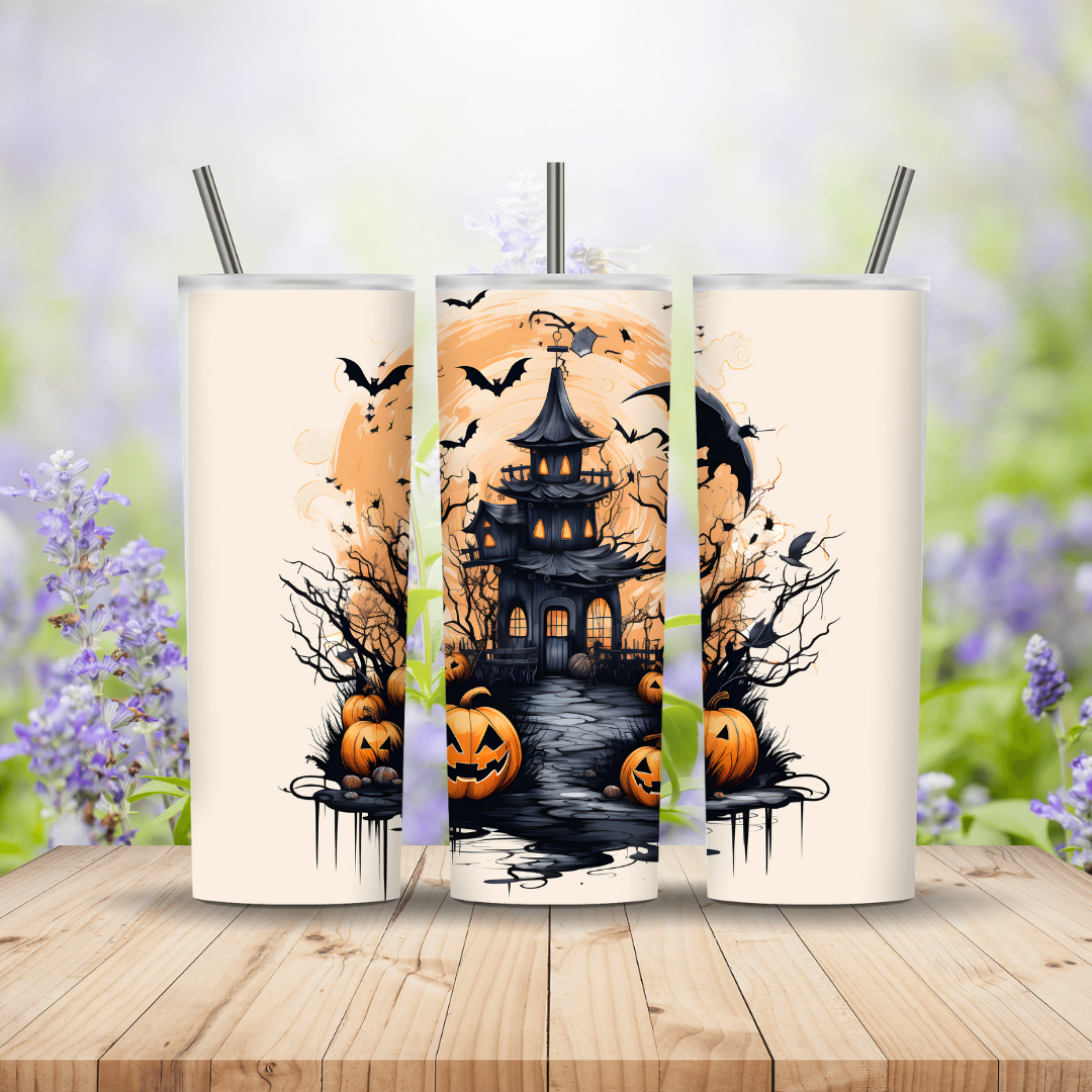 Three Halloween-themed tumblers with pumpkins, bats, and a haunted house design on a wooden surface with a blurred floral background.