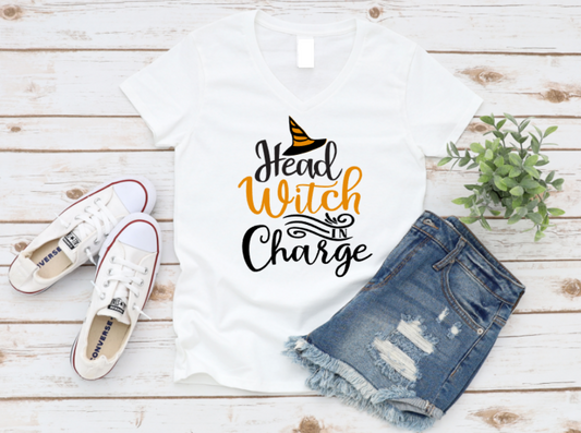 White t-shirt with 'Head Witch Charge' text, denim shorts, and white sneakers on a wooden surface.