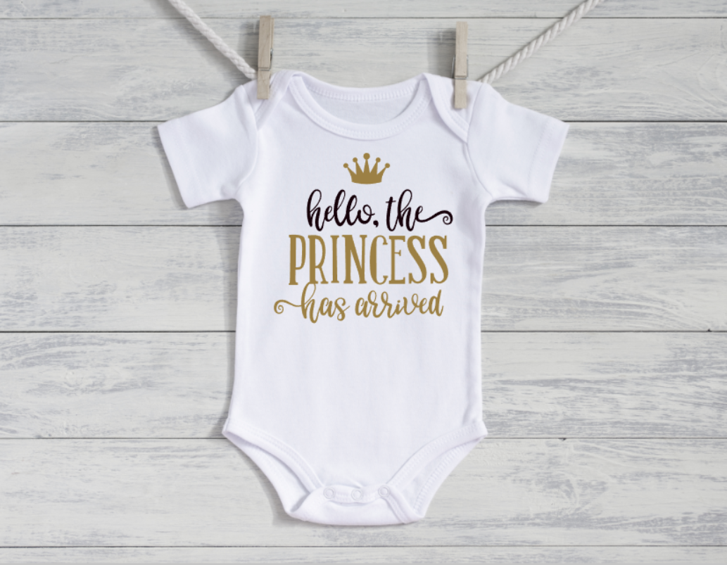 White baby onesie with gold text on a wooden surface