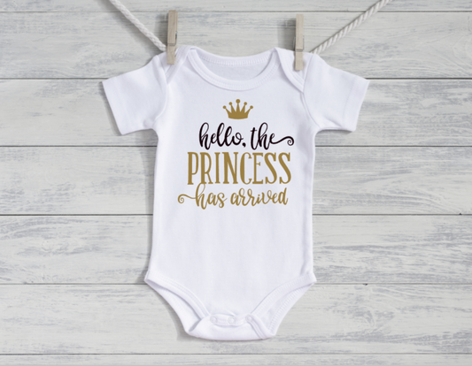 White baby onesie with gold text on a wooden surface