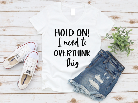 White t-shirt with 'Hold on! I need to overthink this' text, denim shorts, and white sneakers on a wooden surface. www.missmafia.com