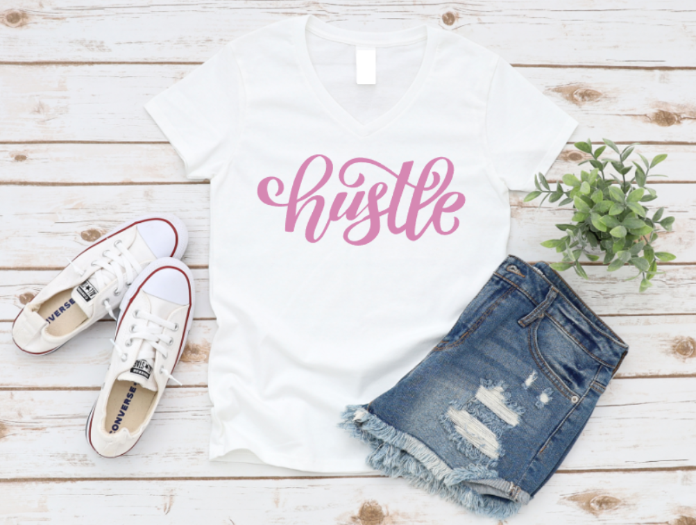 White t-shirt with 'hustle' text, blue jeans, white sneakers, and a plant on a wooden surface.