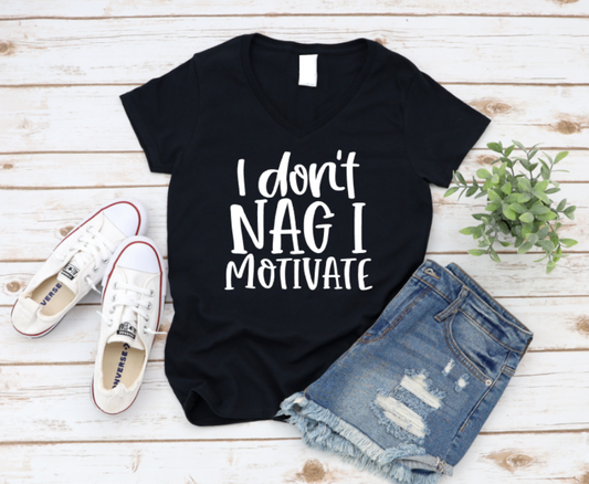 Black unisex t-shirt with bold black text that reads “I Don’t Nag I Motivate, with sneakers and denim shorts on a white flat lay