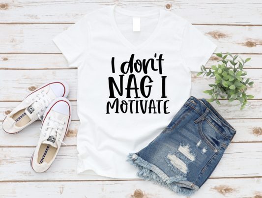 White t-shirt with 'I don't nag I motivate' text, denim shorts, and white sneakers on a wooden surface.