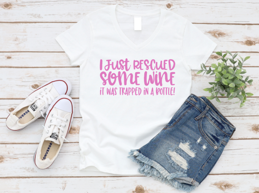 White t-shirt with humorous text, white sneakers, and denim shorts on a wooden surface.