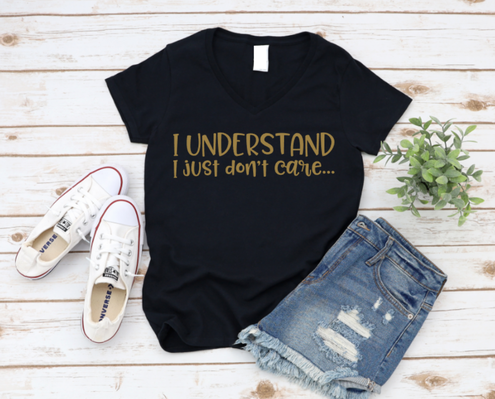 Black t-shirt with 'I UNDERSTAND I JUST DON'T CARE' text, paired with white sneakers and denim shorts on a wooden surface.
