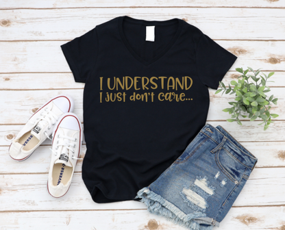 Black t-shirt with 'I UNDERSTAND I JUST DON'T CARE' text, paired with white sneakers and denim shorts on a wooden surface.
