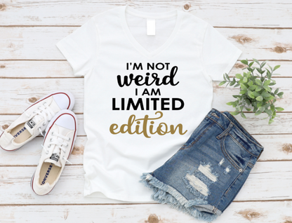White t-shirt with 'I'm not weird, I am limited edition' text, white sneakers, and denim shorts on a wooden surface. www.missmafia.com