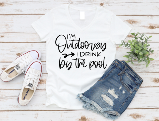 White t-shirt with 'I'm Outdoorsy I Drink by the Pool' text, paired with denim shorts and white sneakers on a wooden surface. www.missmafia.com