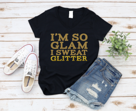 Black t-shirt with 'I'm so glam I sweat glitter' text, paired with denim shorts and white sneakers on a wooden surface. www.missmafia.com