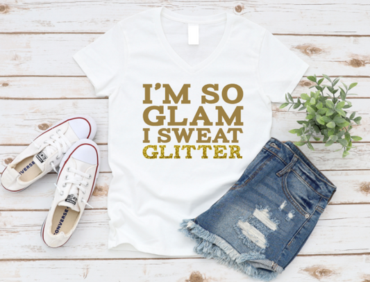 White t-shirt with 'I'm so glam I sweat glitter' text, denim shorts, and white sneakers on a wooden surface. www.missmafia.com