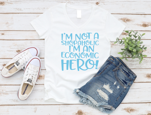 White t-shirt with 'I'm not a shopaholic, I'm an economic hero!' text, denim shorts, white sneakers on a wooden surface. www.missmafia.com