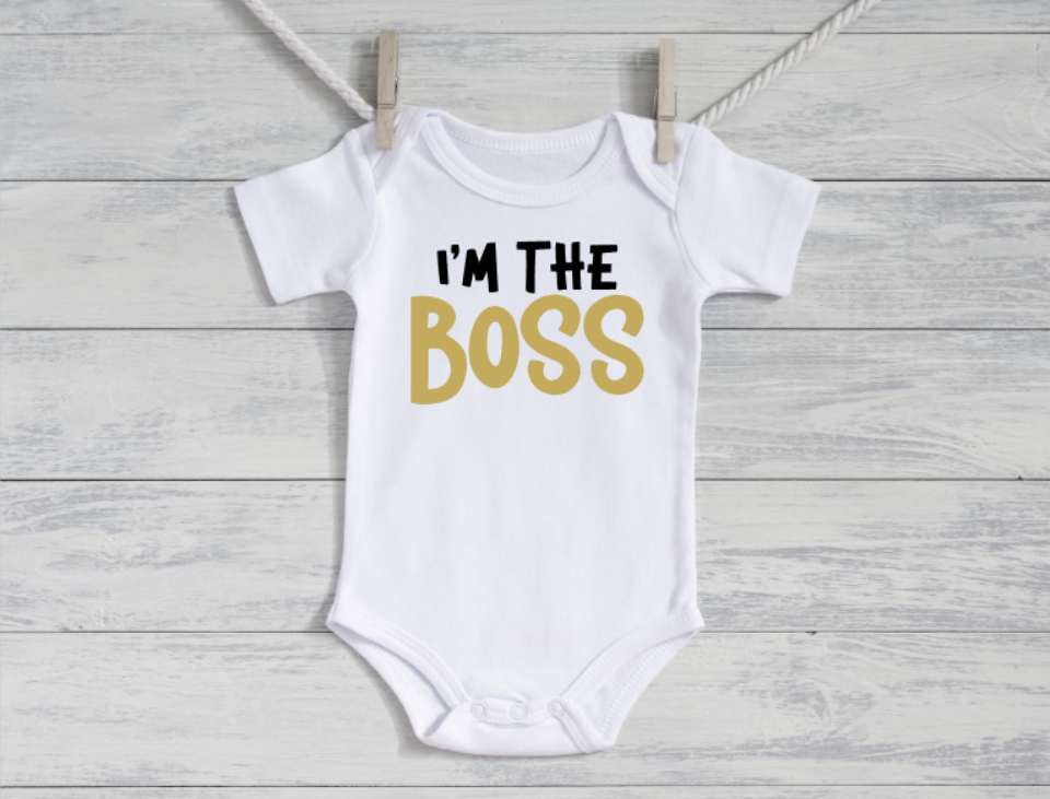 White baby onesie with 'I'm the Boss' text on a wooden surface