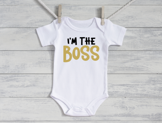 White baby onesie with 'I'm the Boss' text on a wooden surface