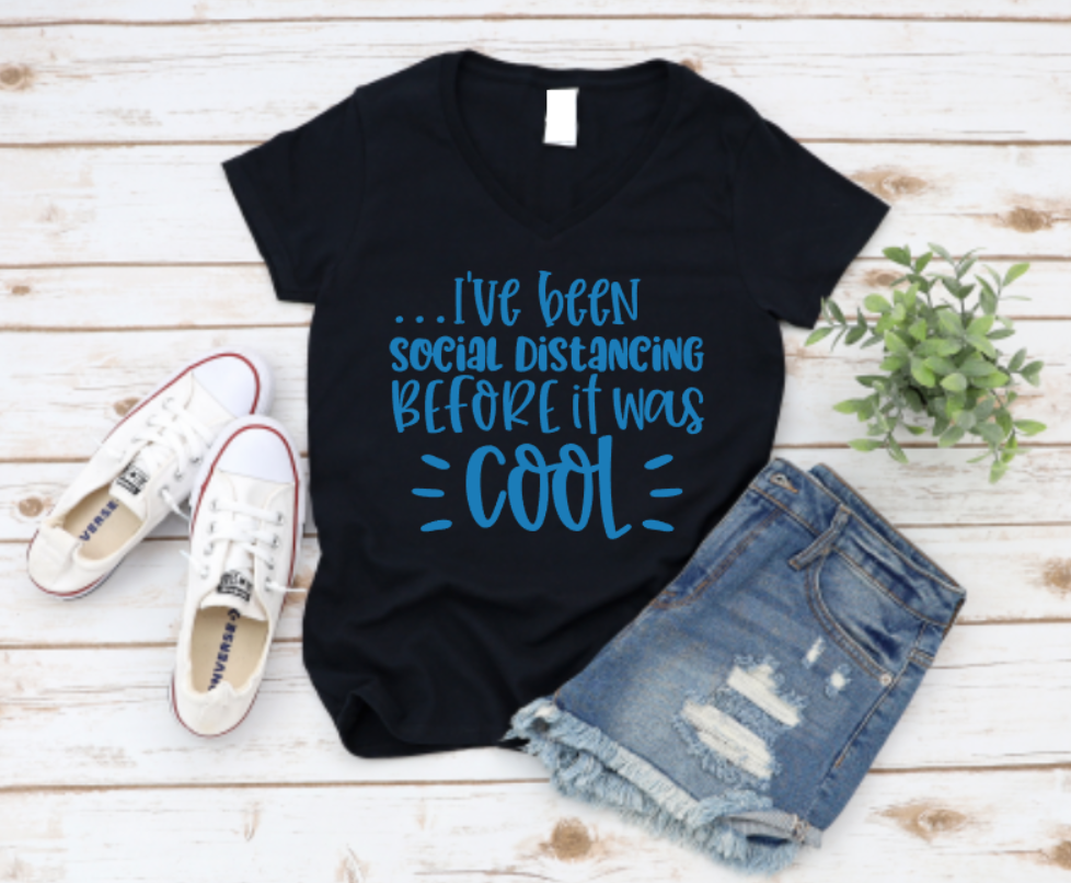 Black t-shirt with blue text 'I've been social distancing BEFORE it was COOL' on a wooden surface with shoes and shorts. www.missmafia.com