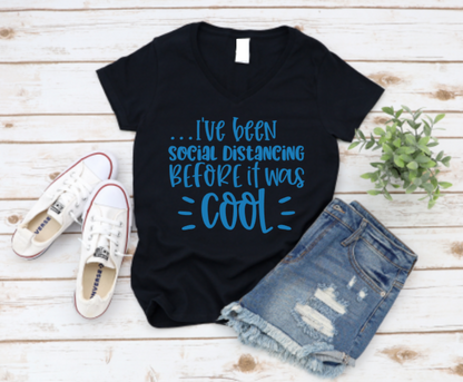 Black t-shirt with blue text 'I've been social distancing BEFORE it was COOL' on a wooden surface with shoes and shorts. www.missmafia.com