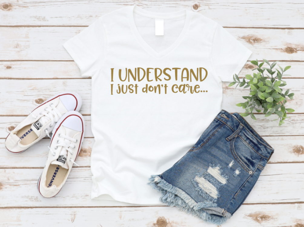 White t-shirt with 'I UNDERSTAND I JUST DON'T CARE...' text, denim shorts, and white sneakers on a wooden surface.