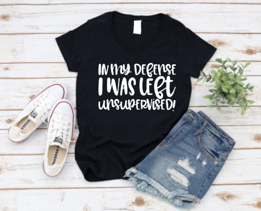 Black t-shirt with 'In my defense I was left unsupervised' text, paired with denim shorts and white sneakers on a wooden surface. www.missmafia.com