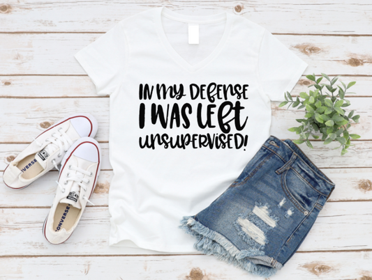 White t-shirt with 'In my defense I was left unsupervised!' text, denim shorts, and white sneakers on a wooden surface. www.missmafia.com