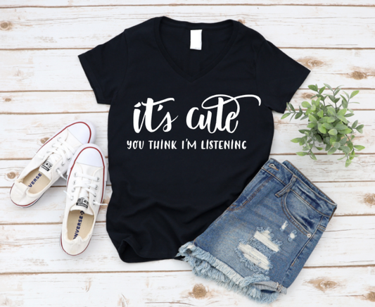 Black t-shirt with 'it's cute you think I'm listening' text, paired with denim shorts and white sneakers on a wooden surface. www.missmafia.com