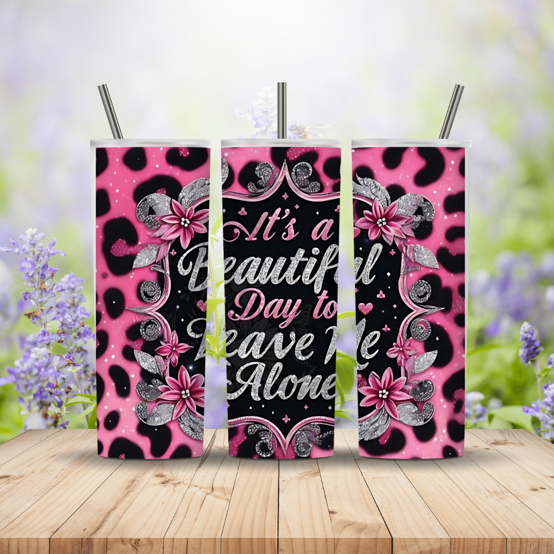 Three pink and black patterned tumblers with floral designs on a wooden surface with blurred flowers in the background.