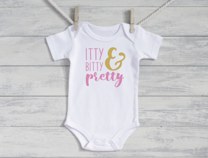 White baby onesie with 'itty bitty & pretty' text on a wooden surface