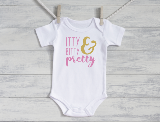 White baby onesie with 'itty bitty & pretty' text on a wooden surface