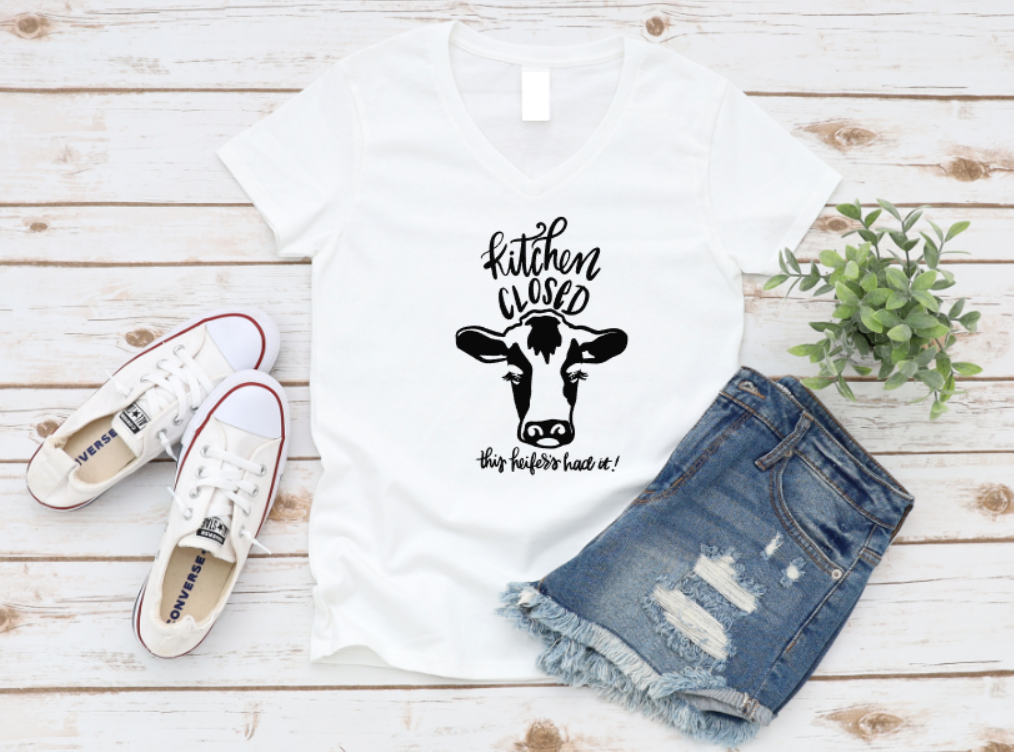 White t-shirt with cow graphic and text, paired with denim shorts and sneakers on a wooden surface.