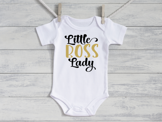 White baby onesie with 'Little Boss Lady' text on a wooden surface