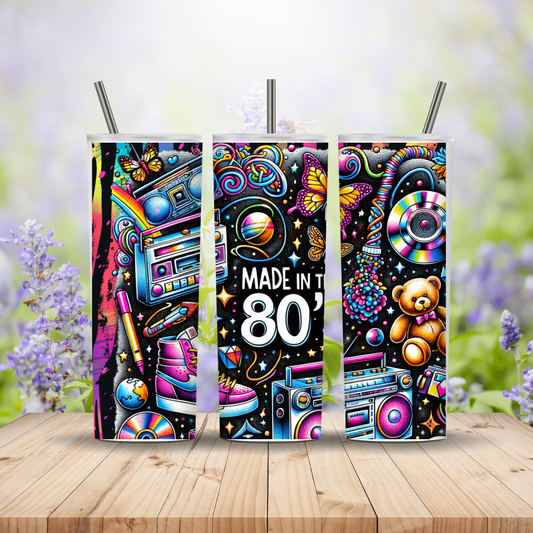 Three colorful tumblers with 80s-themed designs on a wooden surface with a blurred floral background.