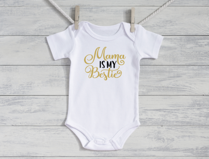 White baby onesie with 'Mama is my Bestie' text in gold on a wooden surface.