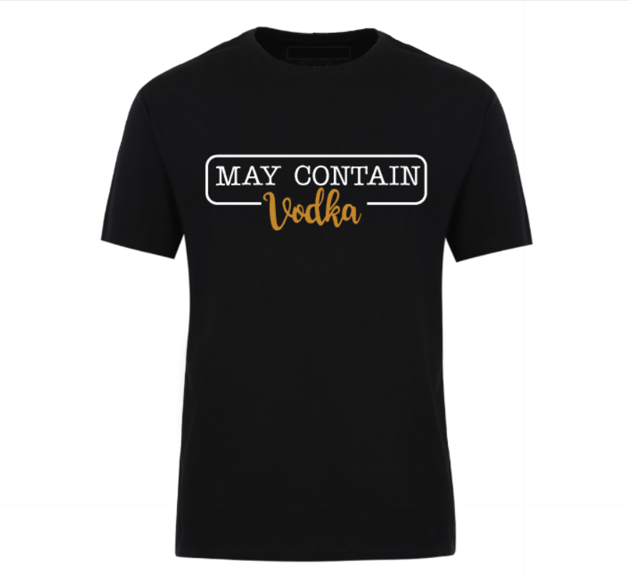 Flat lay of a black t-shirt with the phrase “May Contain Vodka” in black and gold text, styled with denim shorts and white Converse sneakers on a wooden background.