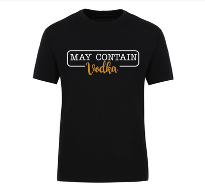 Flat lay of a black t-shirt with the phrase “May Contain Vodka” in black and gold text, styled with denim shorts and white Converse sneakers on a wooden background.